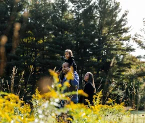 A dad carries his child on his shoulders while walking through a park with his partner