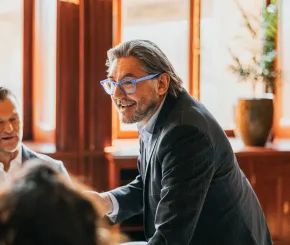 A man in a suit and blue glasses speaks to a group of charity trustees