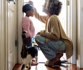 A mother marking her daughter's height, with their pet cat in the foreground