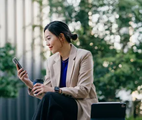Female sitting outside on bench with coffee checking mobile phone