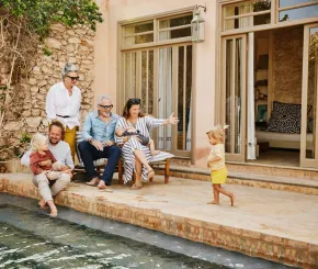 Three generations of a family relax by the pool of a luxurious house