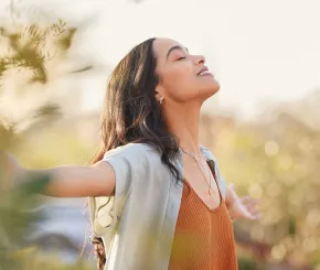 image of a woman at peace in an idyllic scene outdoors in nature standing with arms spread wide with a sense of freedom