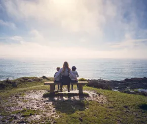 mother and child resting on a bench on a sunny summer's afternoon overlooking the blue sea