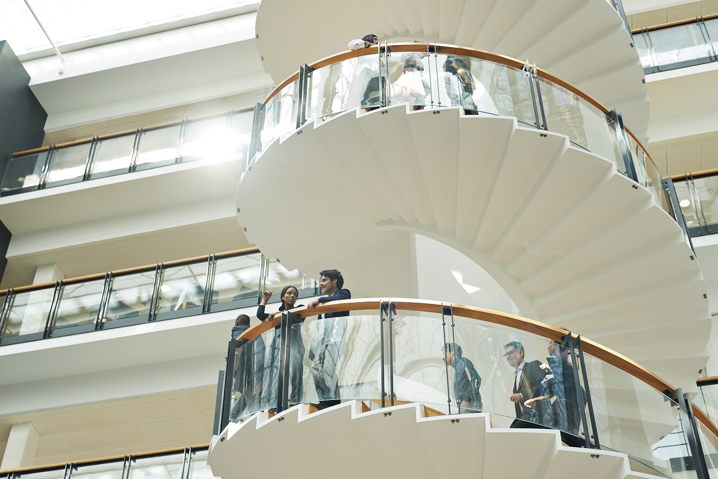 People stand on a spiral staircase looking outwards in a large building