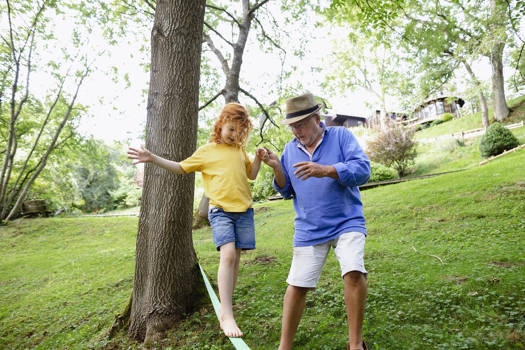 Grandfather holding the hand of his granddaughter as she is slacklining