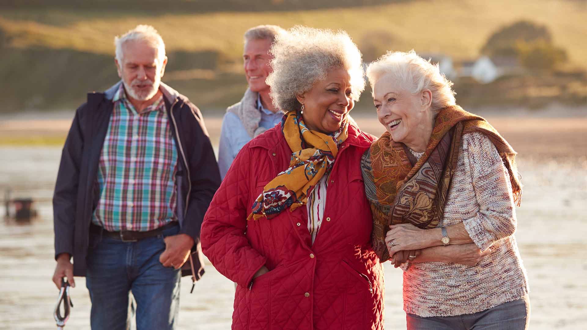 image of windswept elderly individuals walking arm in arm along a beach
