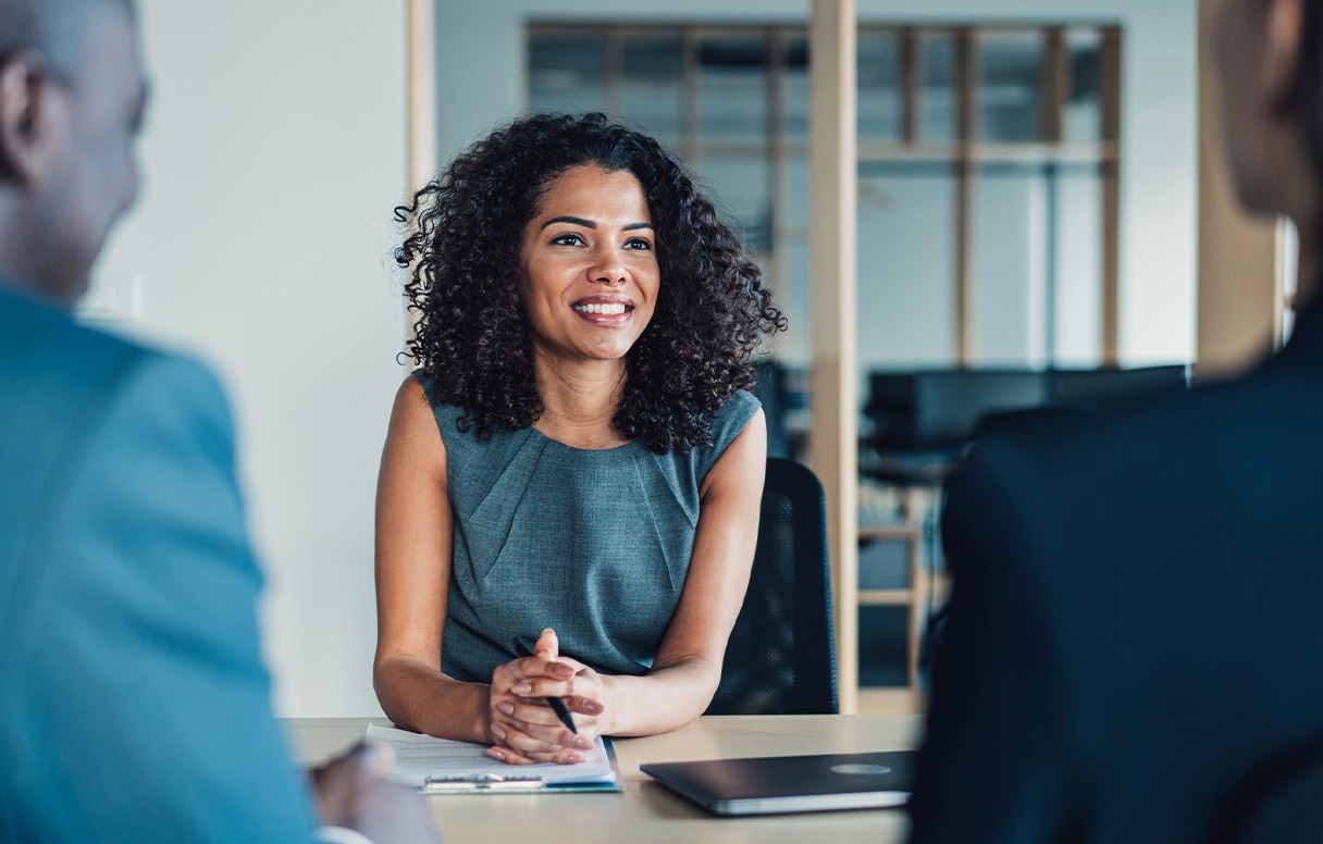 A businesswoman sits in a meeting and speaks to colleagues